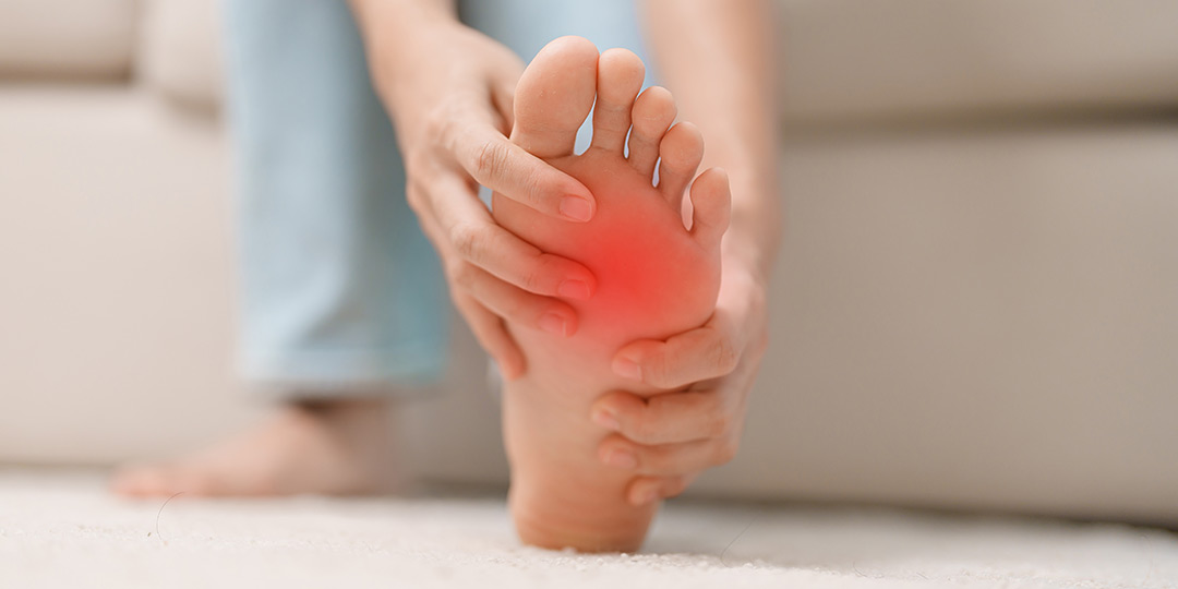 Woman having barefoot pain during sitting on couch at home.